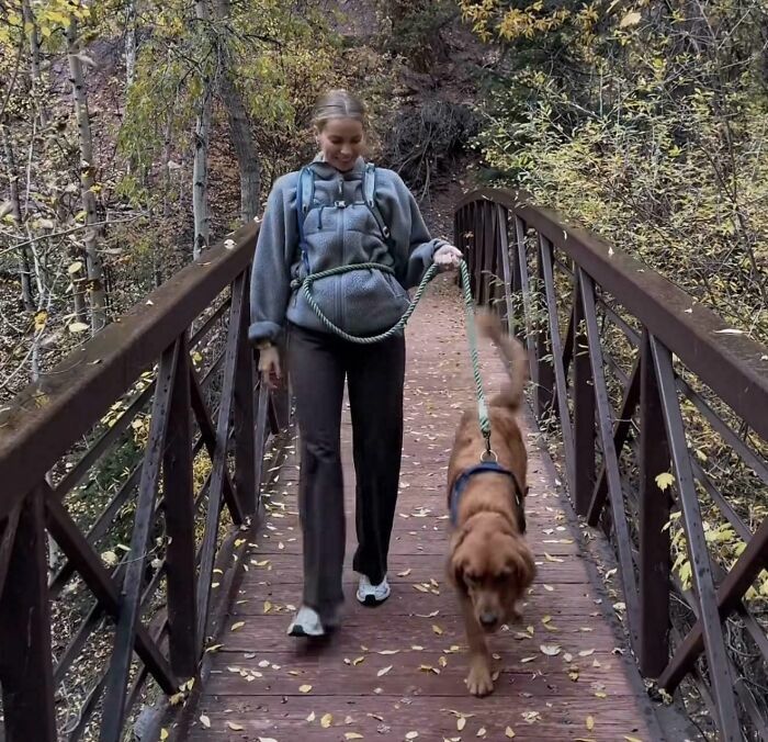 Una de las influencers caminando con su perro por un puente de madera en la naturaleza.