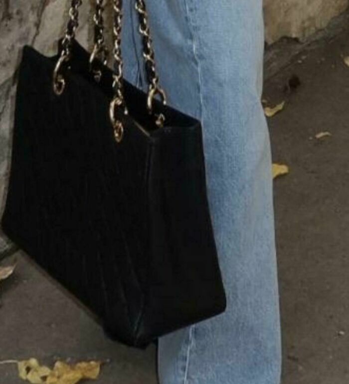 Influencers mostrando un bolso de mano negro con asas de cadena en la calle.