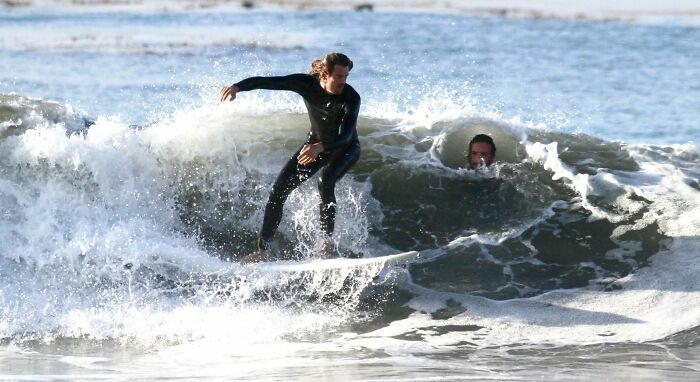 Surfista en la ola mientras otro aparece al fondo en fotos divertidas