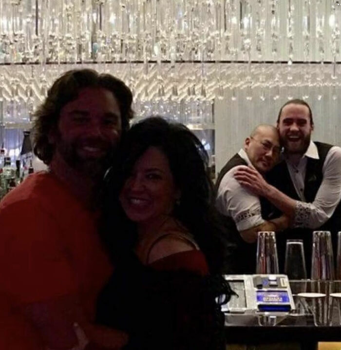 Pareja sonriendo mientras en el fondo se ve una escena graciosa, una de esas fotos divertidas con un fondo inesperado.