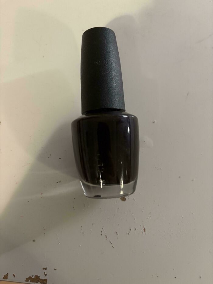 Frasco de esmalte de uñas oscuro sobre una superficie, mostrando fallos de diseño