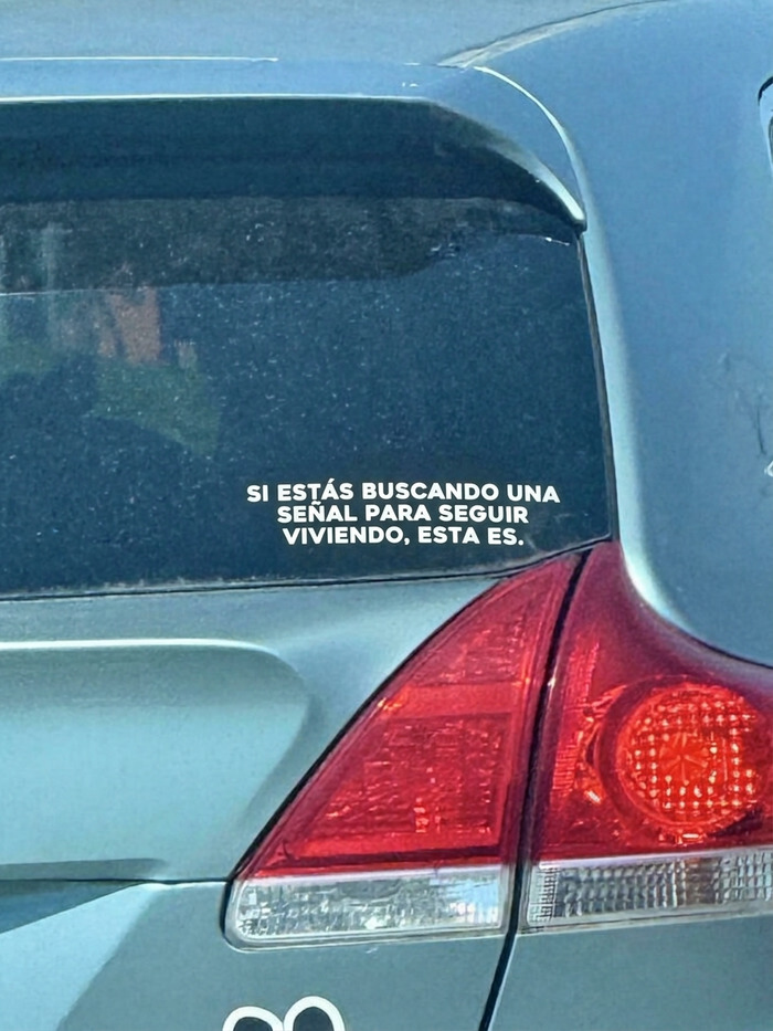 Un coche con pegatinas en los parachoques que incluye un mensaje positivo para seguir viviendo.