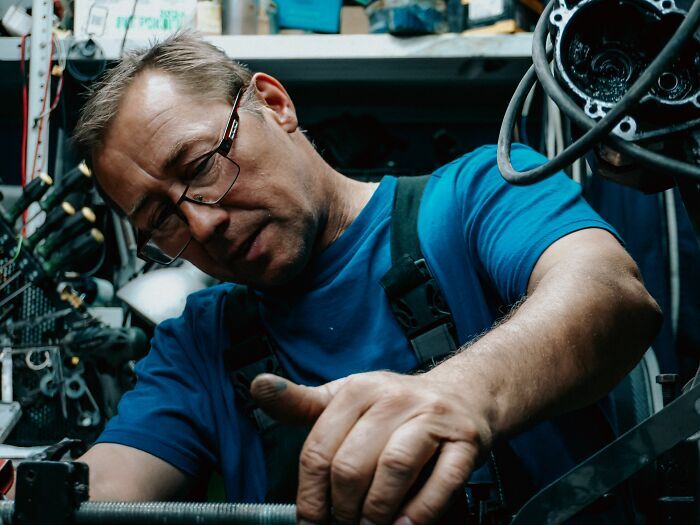 Un hombre con gafas trabajando atentamente en un taller mecánico antes de ser uno de los trabajadores despedidos.