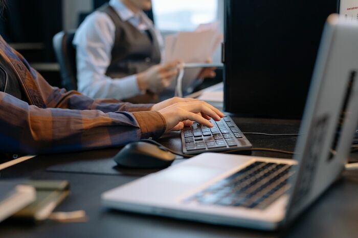 Manos de trabajadores escribiendo en un teclado dentro de una oficina.
