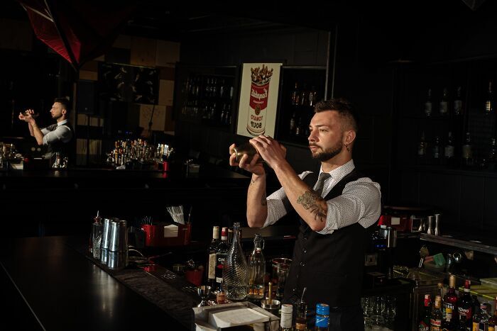 Un bartender preparando una bebida en un bar oscuro, representando a trabajadores despedidos.