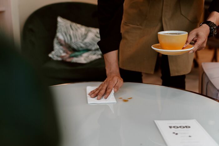 Camarero limpiando una mesa mientras sostiene café, experiencia de trabajadores que fueron despedidos casi inmediatamente.