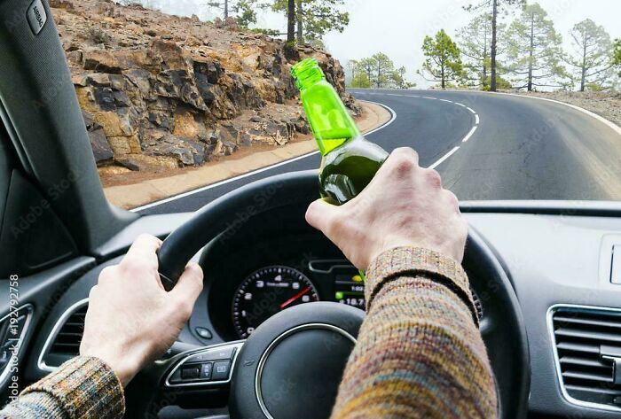 Conductor sosteniendo una botella frente a una curva, ejemplo de mentiras ridiculas publicadas en internet.