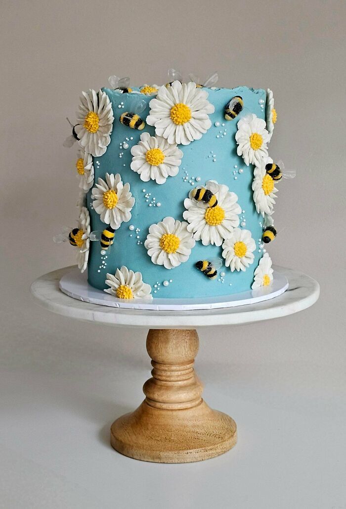 Pastel azul decorado con margaritas y abejas, muestra de repostería creativamente elaborada.