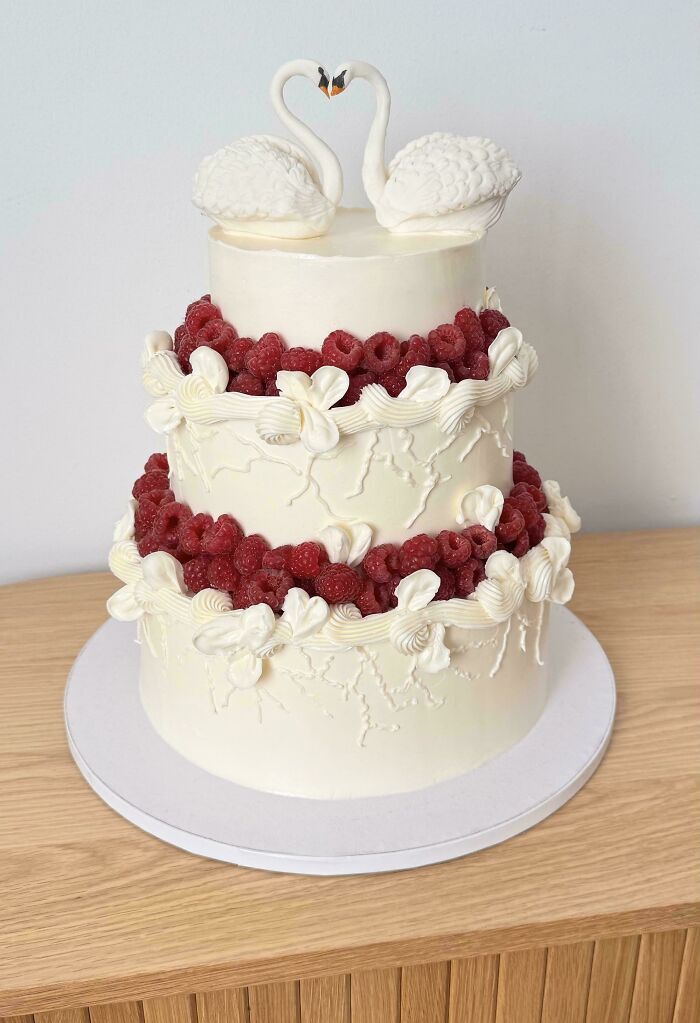 Pastel elegante de bodas decorado con frambuesas frescas y cisnes de repostería.